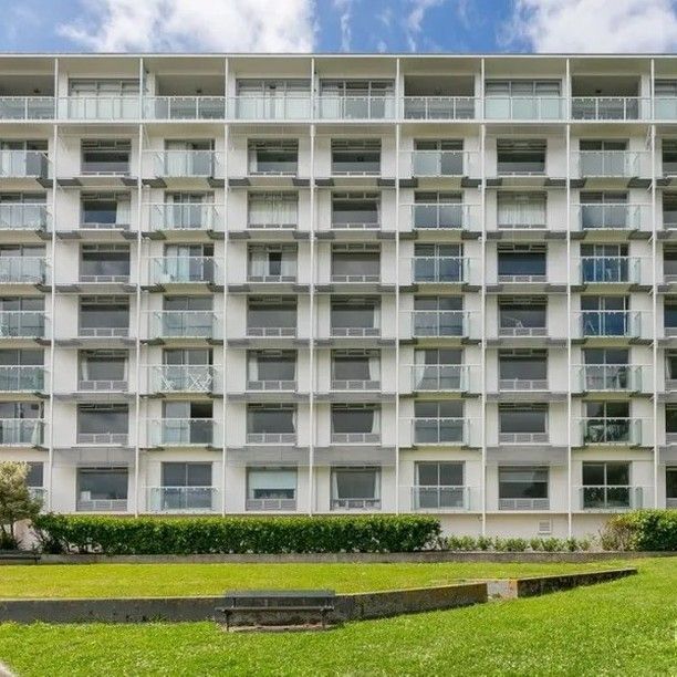 White apartment building with balconies behind a grassy lawn and hedges