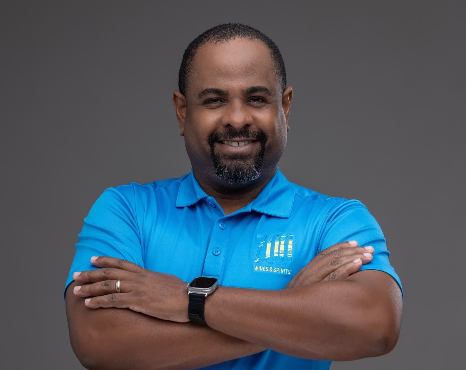 A man wearing a blue shirt and a watch is standing with his arms crossed.