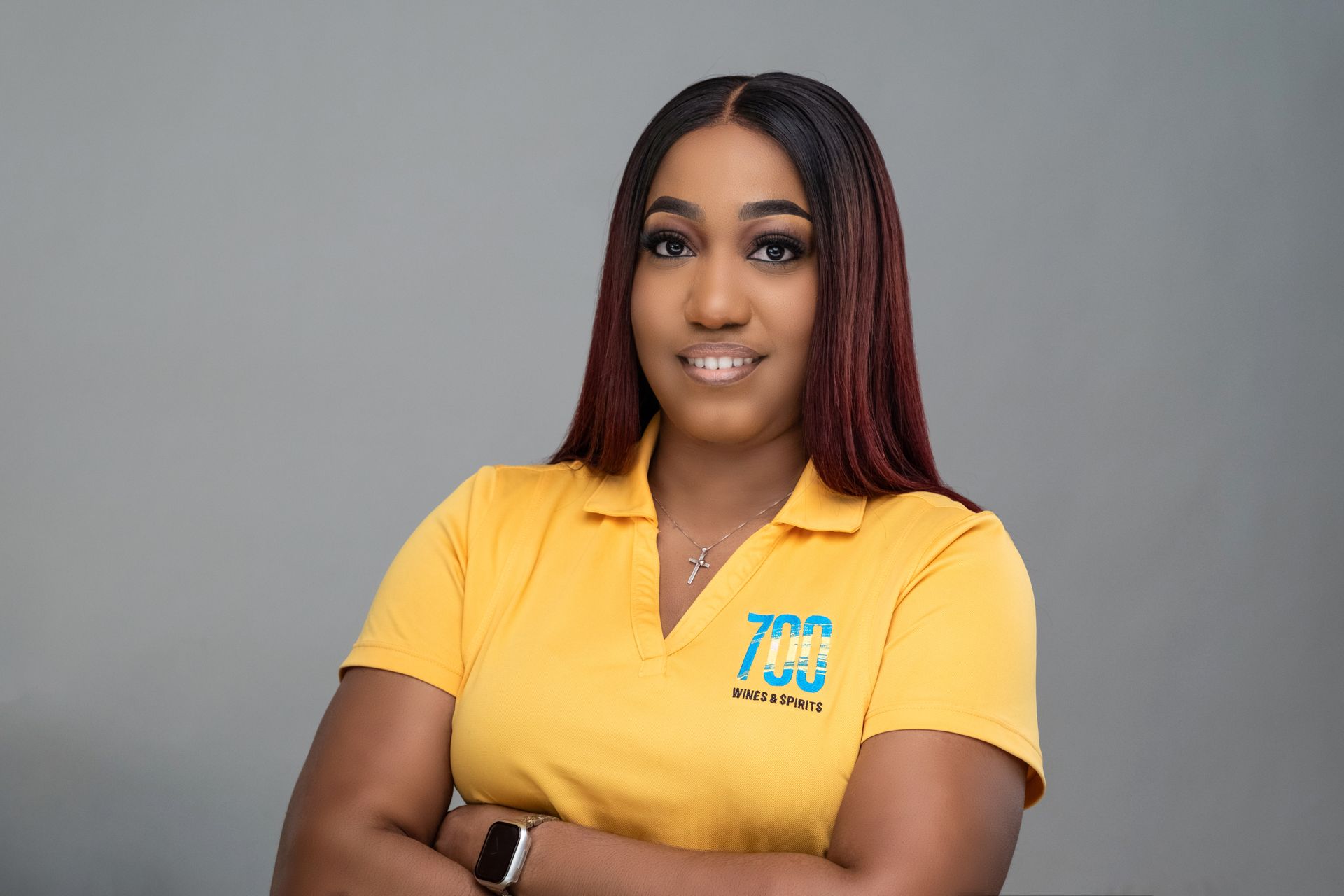 A woman in a yellow shirt is standing with her arms crossed and smiling.
