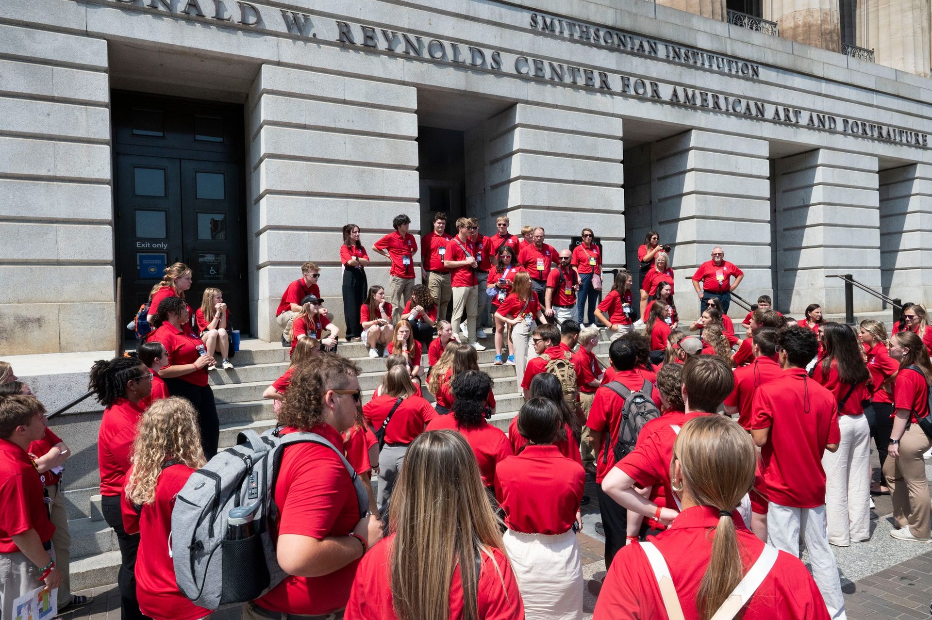A large group of people in red shirts are standing in front of a building.