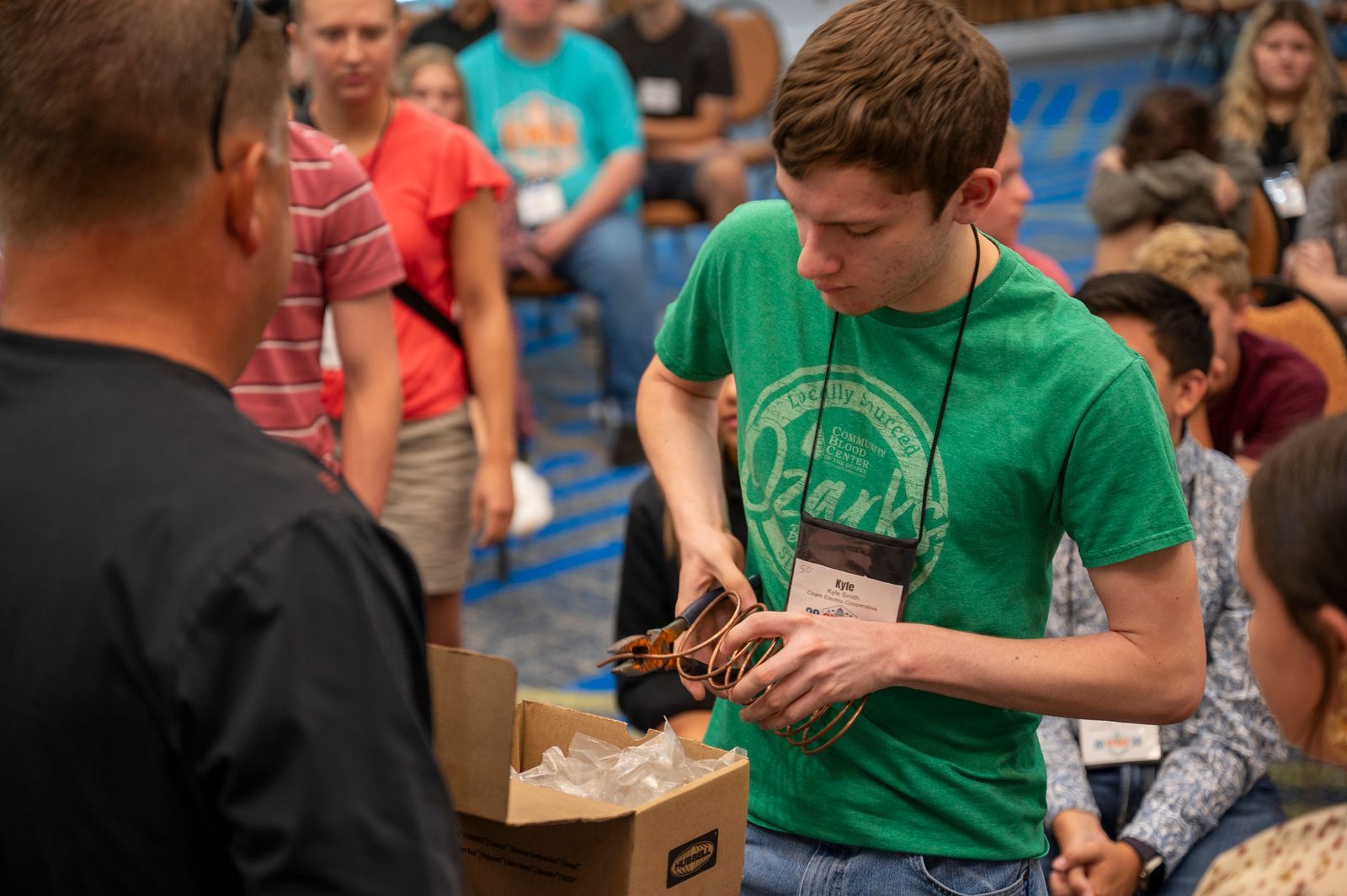 A young man in a green shirt is standing in front of a cardboard box.