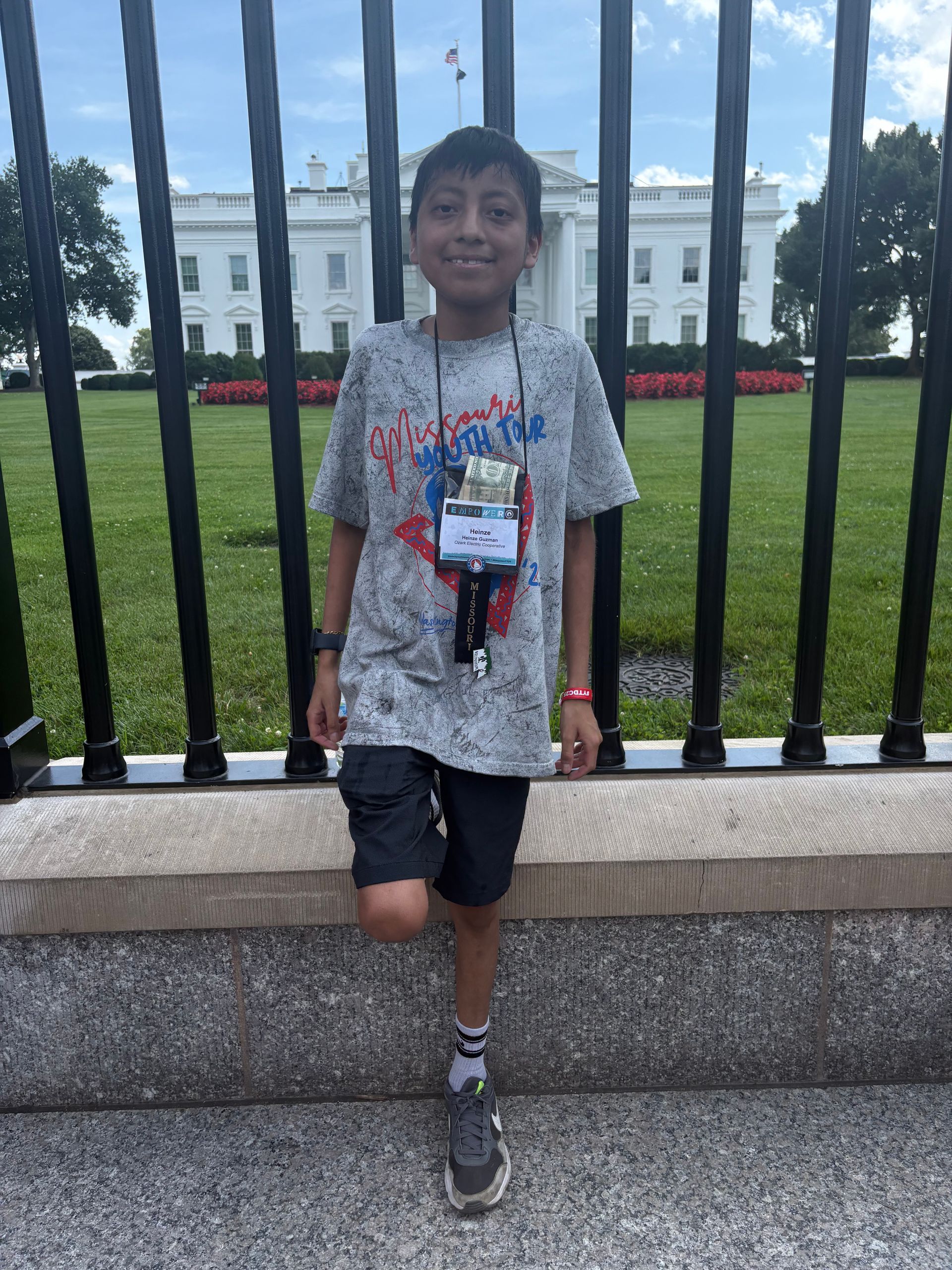Boy standing by a black fence in front of the White House, wearing a name badge