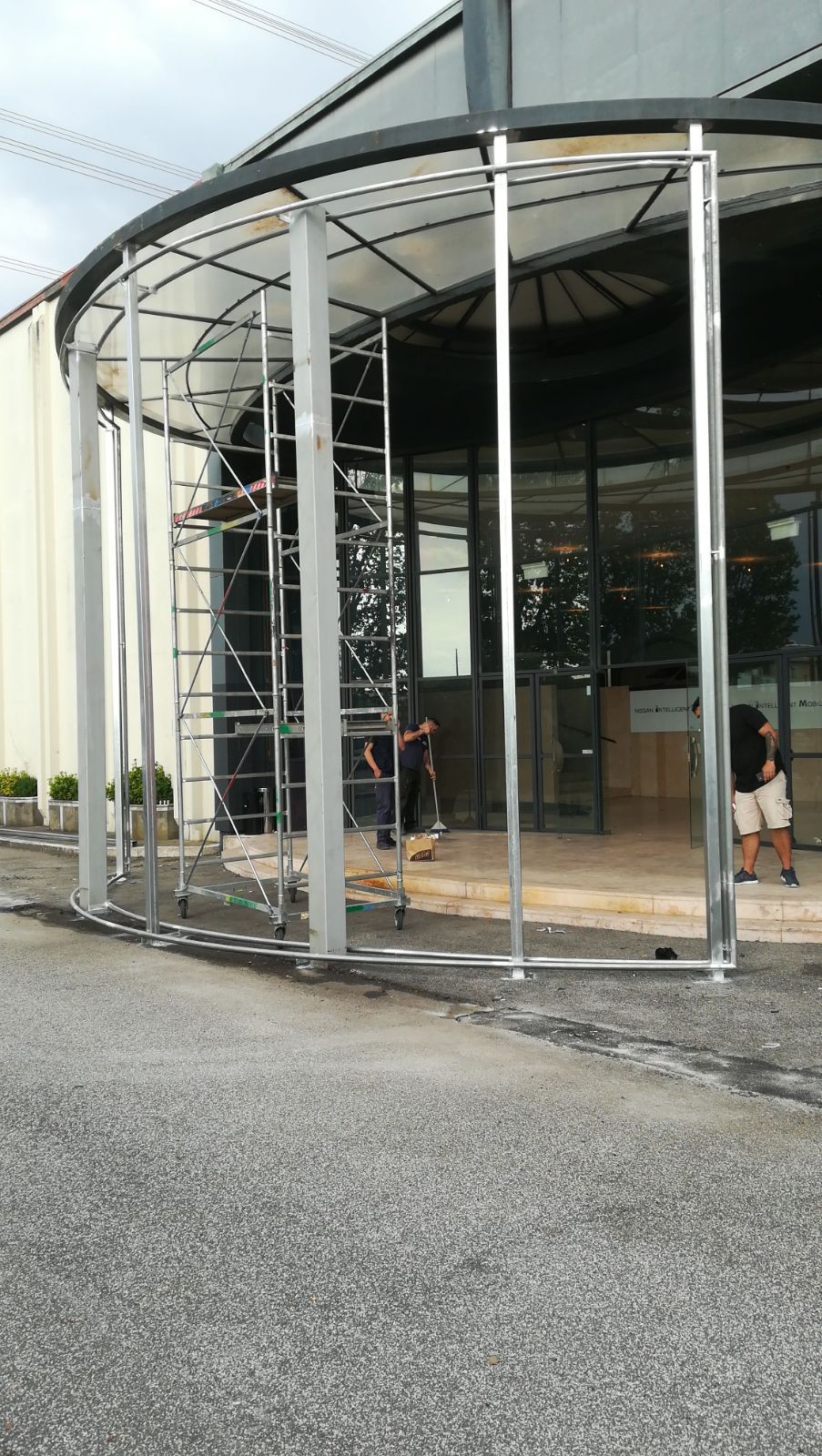 Ingresso in vetro curvo con porte girevoli in un edificio moderno, con due persone vicino all'ingresso