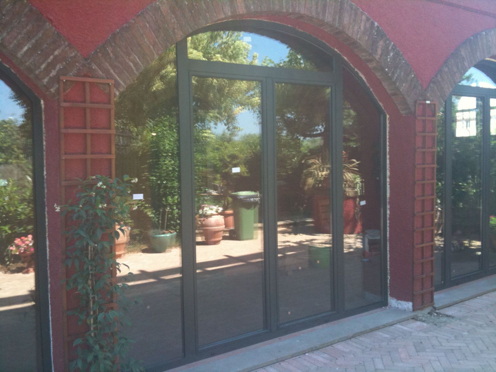 Vetrine scure ad arco in vetro incastonate in un muro di mattoni rossi con piante in vaso all'esterno.
