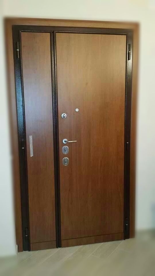 Porta d'ingresso in legno con pannello laterale stretto, inserita in un corridoio beige.