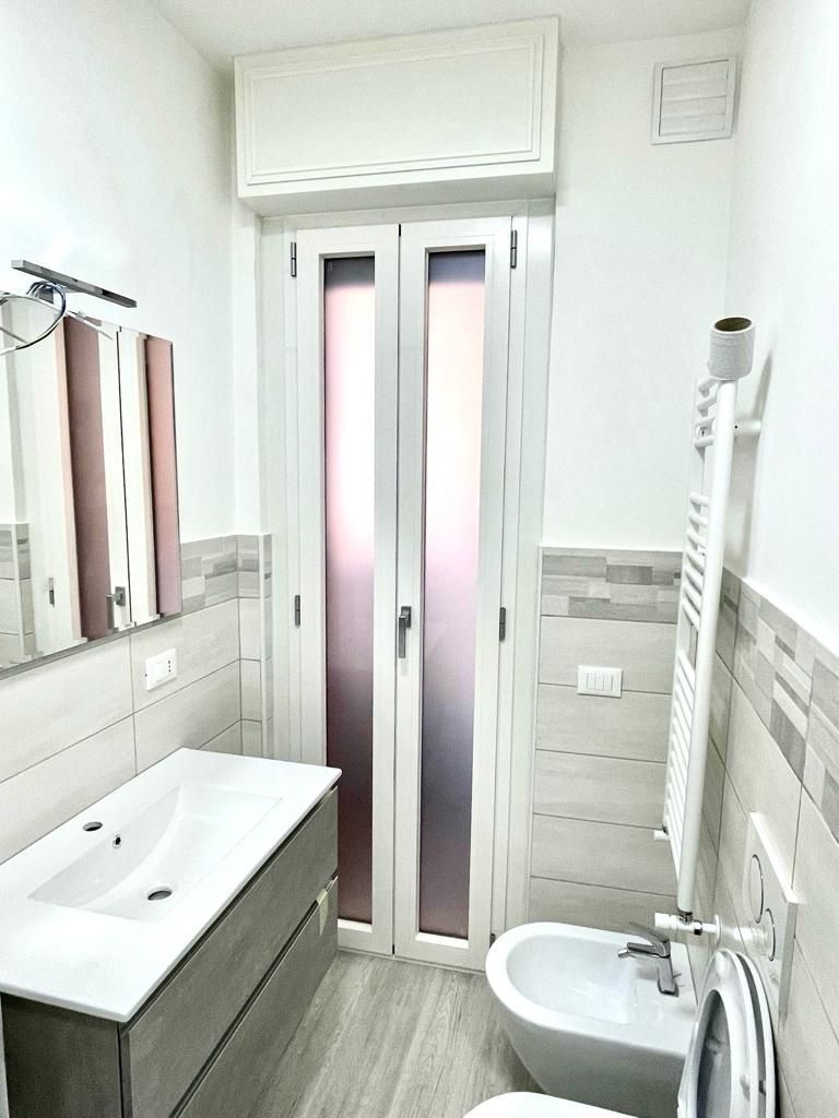 Piccolo bagno moderno con lavabo, WC, doccia e porta in vetro satinato sotto un condizionatore d'aria a parete.