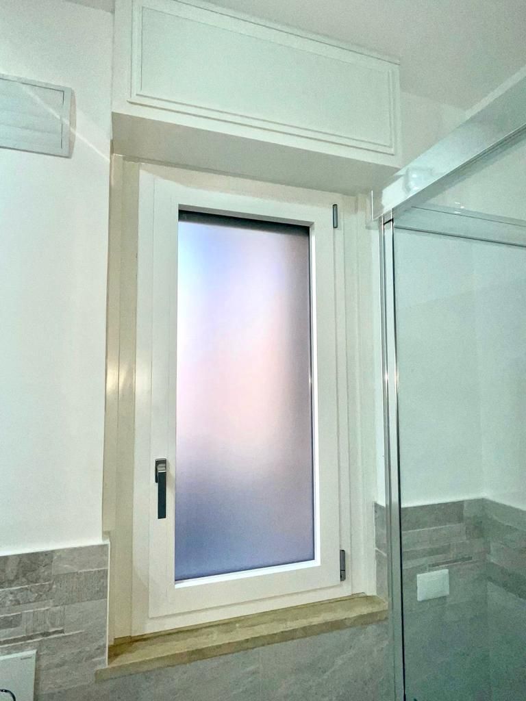 Finestra del bagno con vetro satinato, cornice bianca e pareti piastrellate.