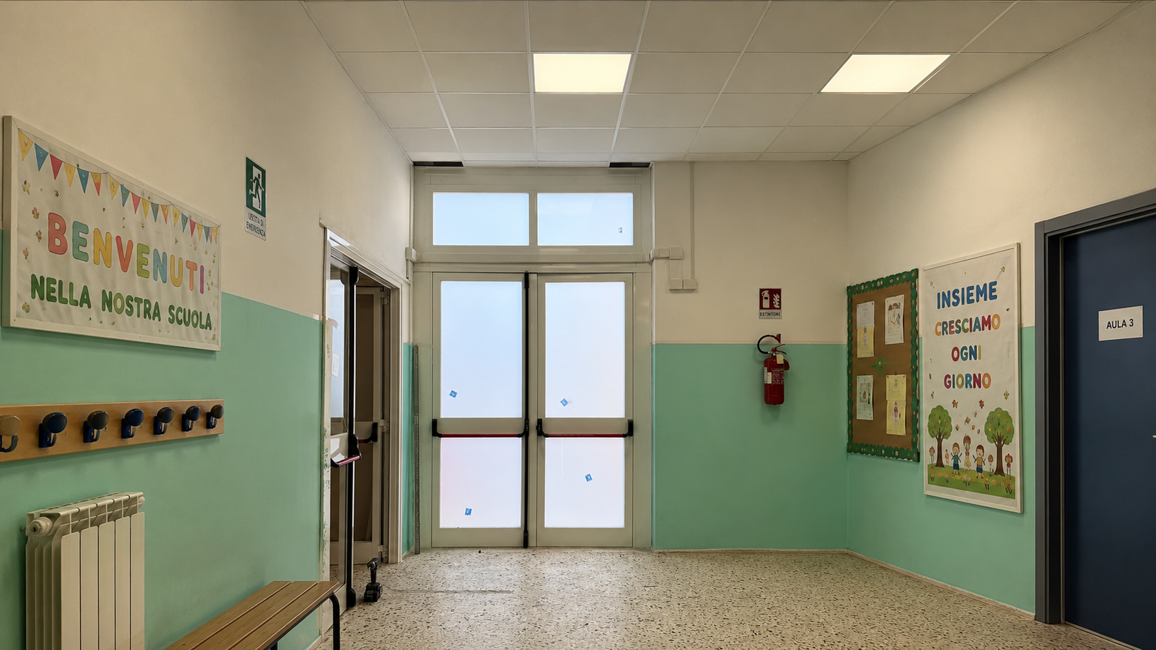 Corridoio scolastico vuoto con pareti verde menta, porte blu, appendiabiti, bacheche e doppie porte in fondo.