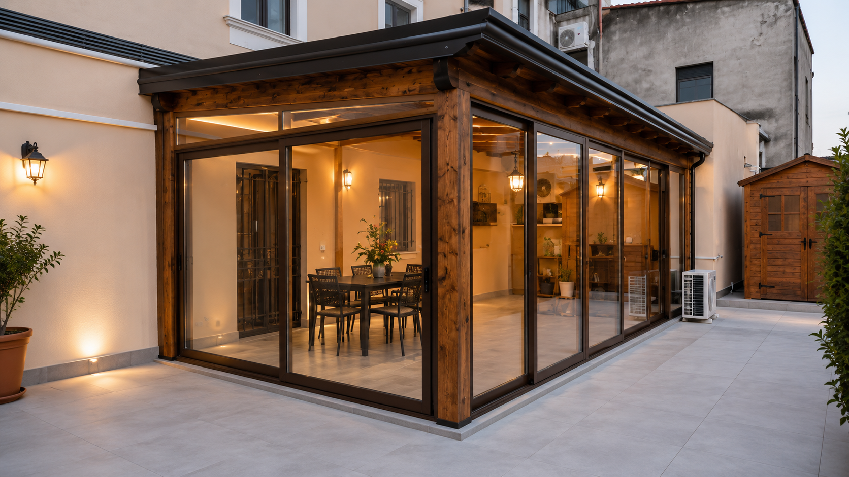 Zona pranzo esterna con vetrate, illuminata da luci soffuse e adiacente a un vialetto che conduce al cortile.