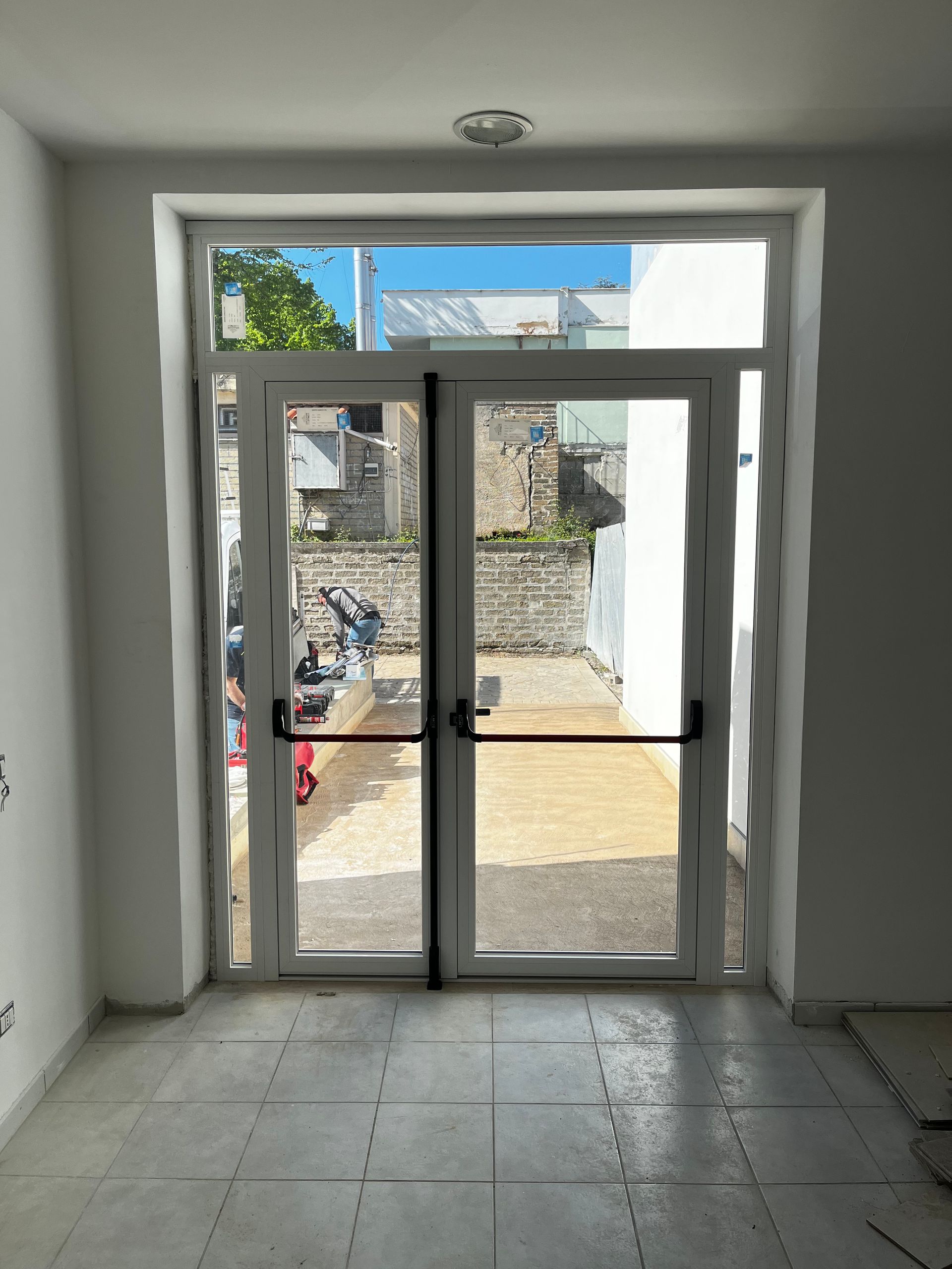 Stanza vuota con pavimento piastrellato, doppie porte finestre aperte e vista su un patio esterno.
