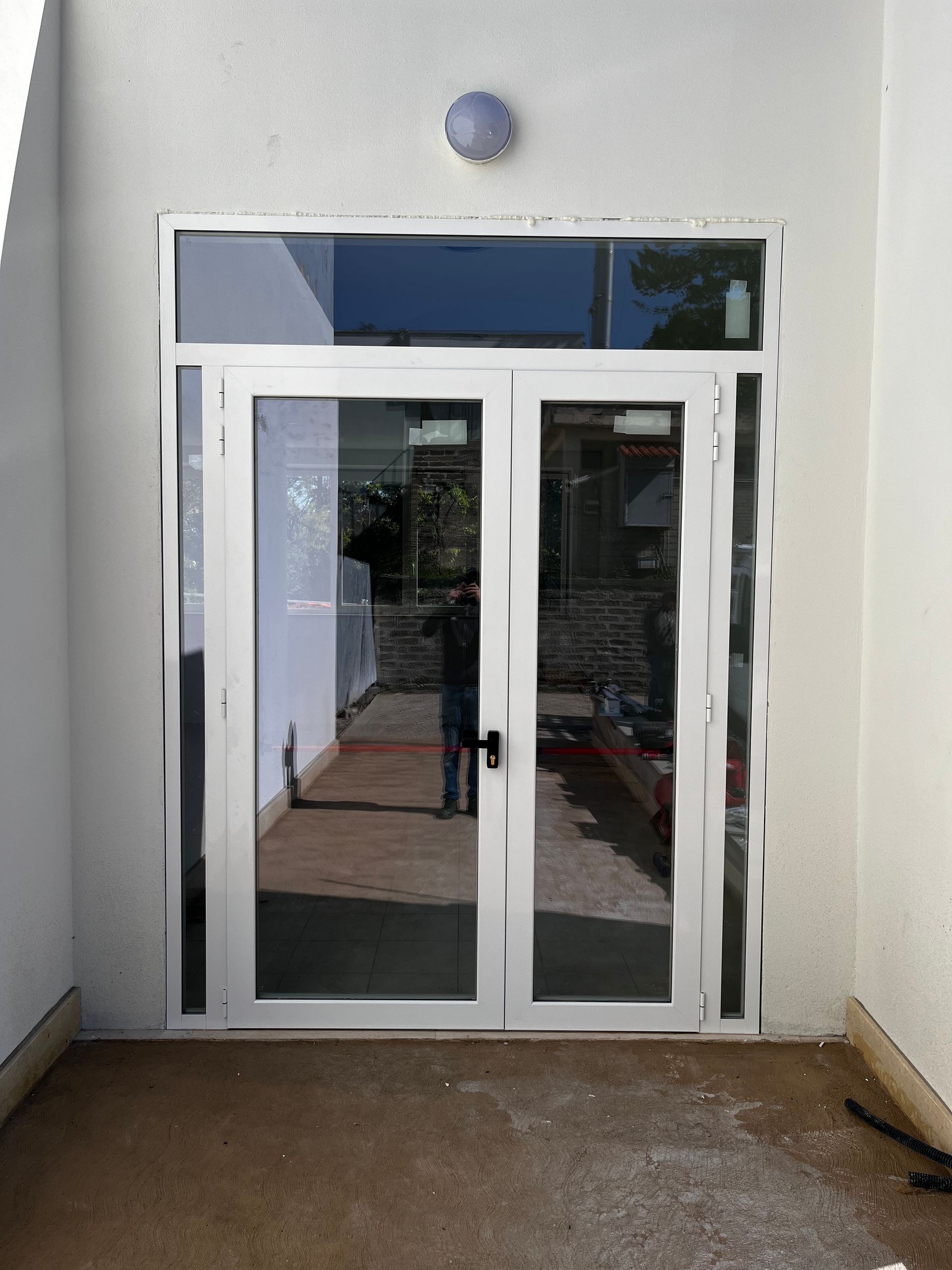 Doppie porte a vetri sotto una finestra circolare all'ingresso di un edificio, con uno stretto passaggio che conduce ad esse.