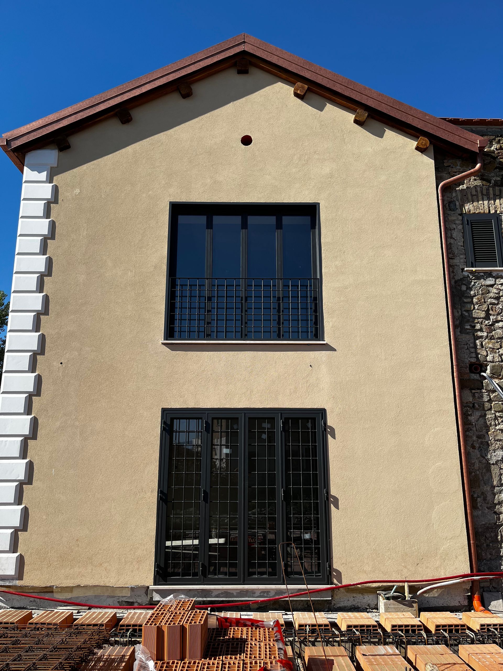 Vista frontale di una casa in muratura con facciata in stucco, finestre nere e tegole rosse.