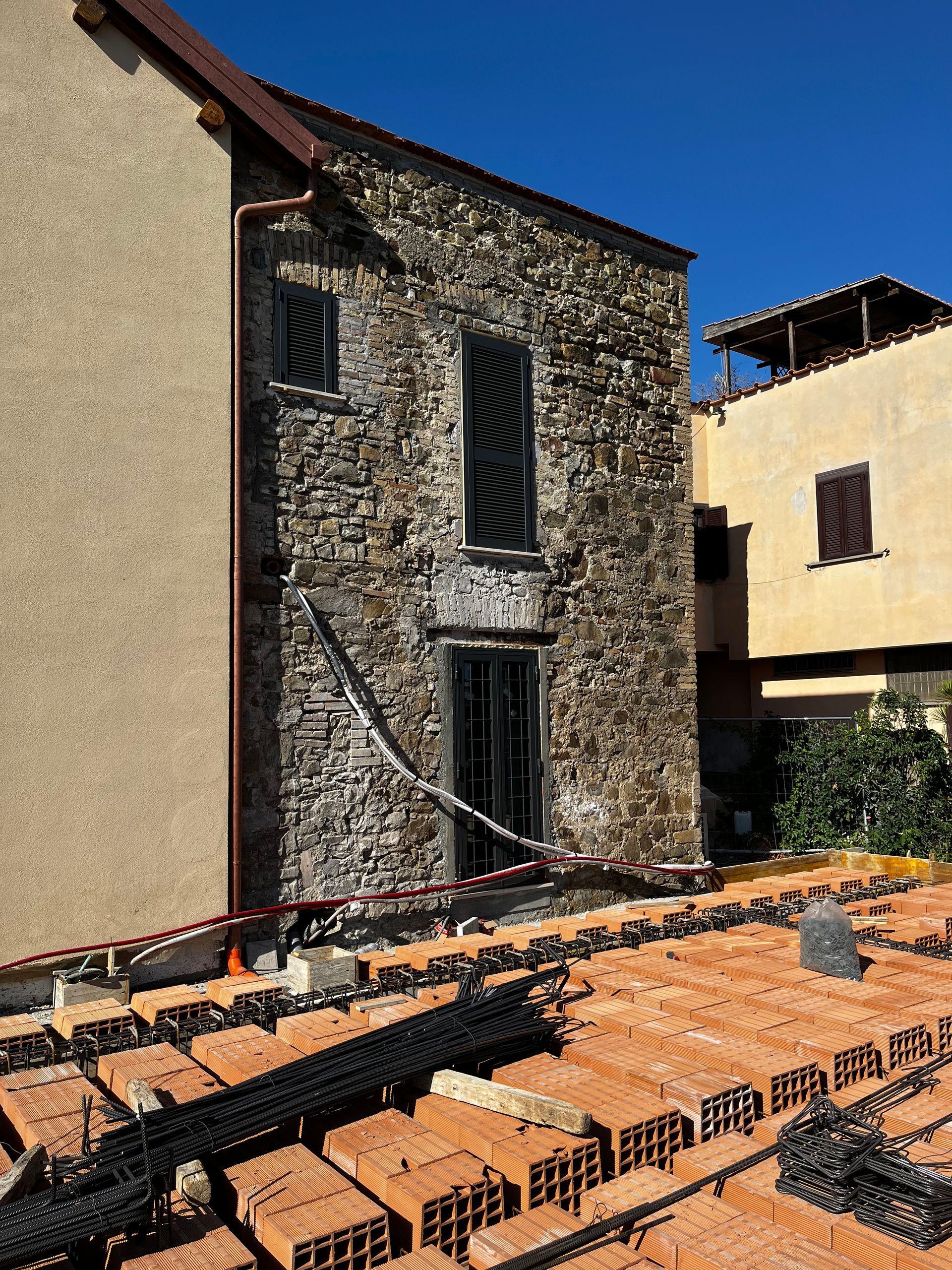 Casa rustica in pietra in fase di ristrutturazione, con mattoni a vista e impalcature sul davanti.