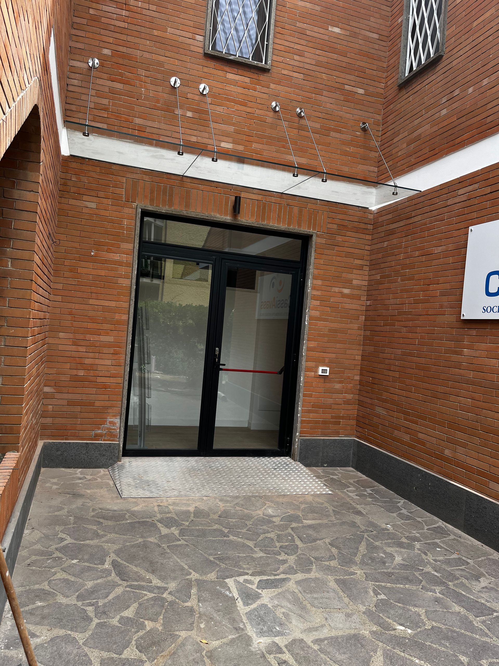 Ingresso dell'edificio in mattoni con doppie porte a vetri e vialetto in pietra.