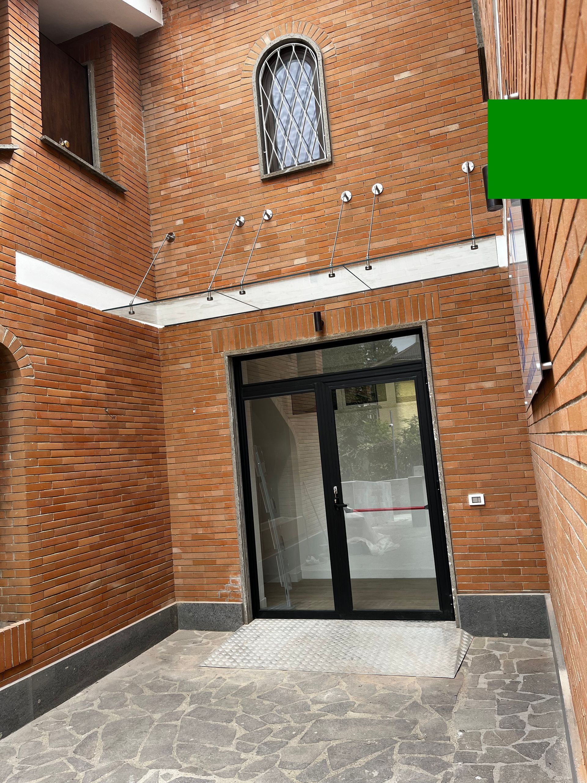 Ingresso in mattoni nel cortile con doppie porte a vetri e finestra ad arco soprastante