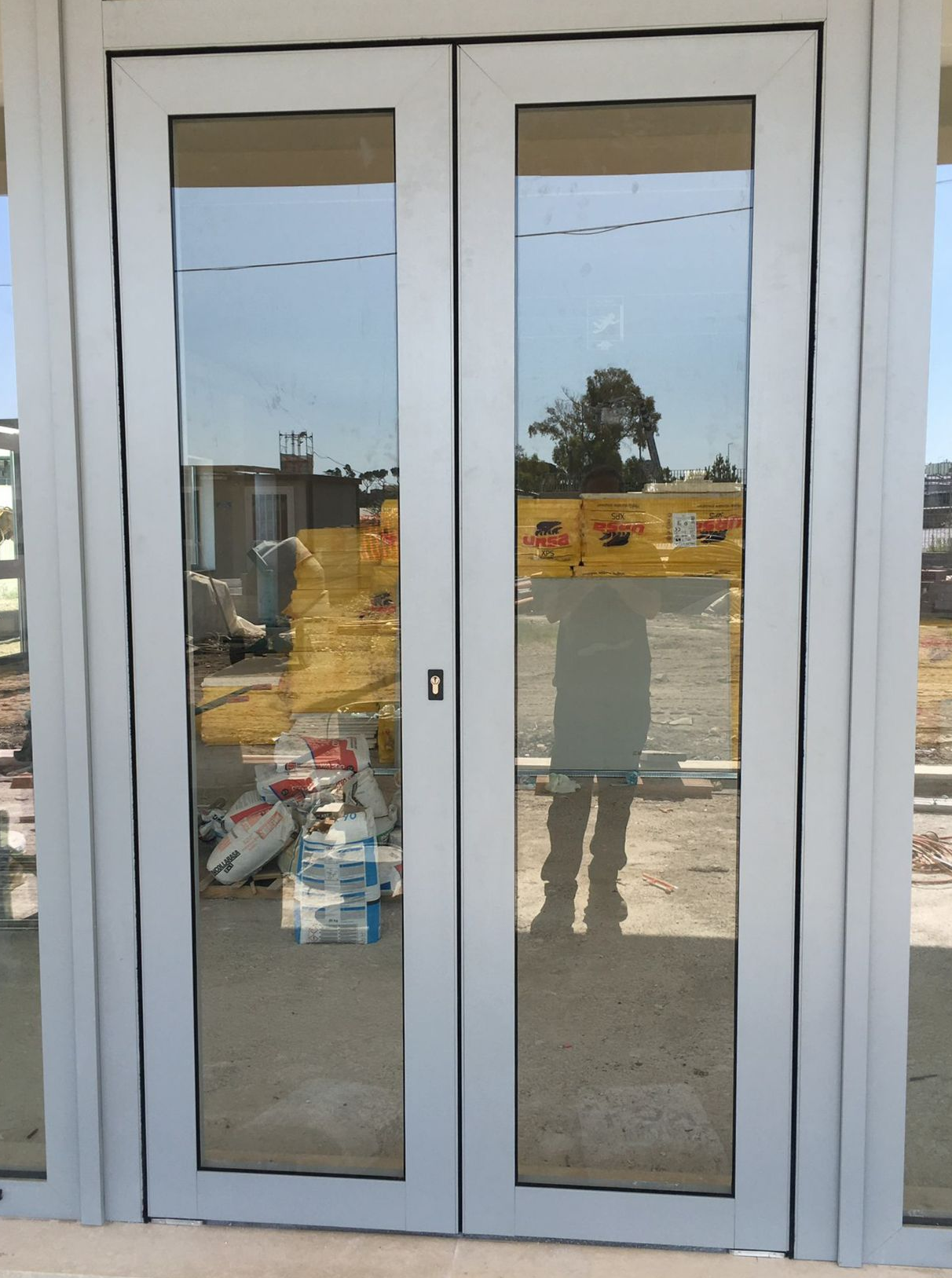 Doppie porte a vetri bianche chiuse, con riflessi di un cantiere edile all'esterno.