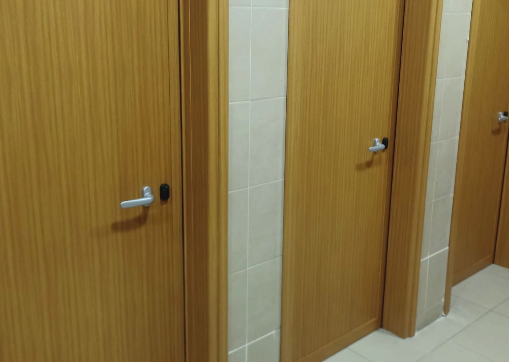 Una fila di porte di legno per i bagni pubblici, con maniglie in metallo, in un corridoio piastrellato.