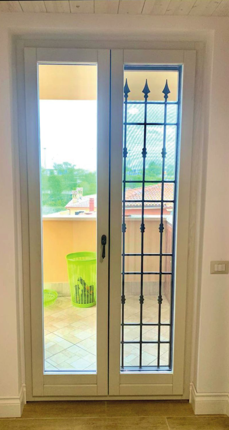Porte finestre bianche con un pannello di vetro stretto e vista sul balcone, in una stanza luminosa