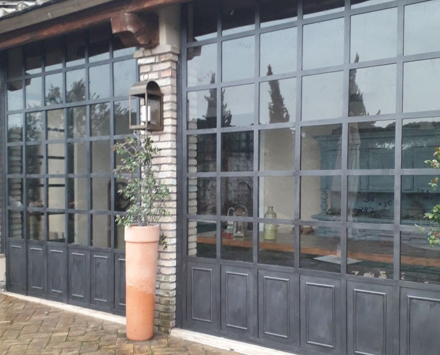 Vetrina con porte e finestre con cornici nere, muro in pietra e una pianta in vaso all'ingresso.