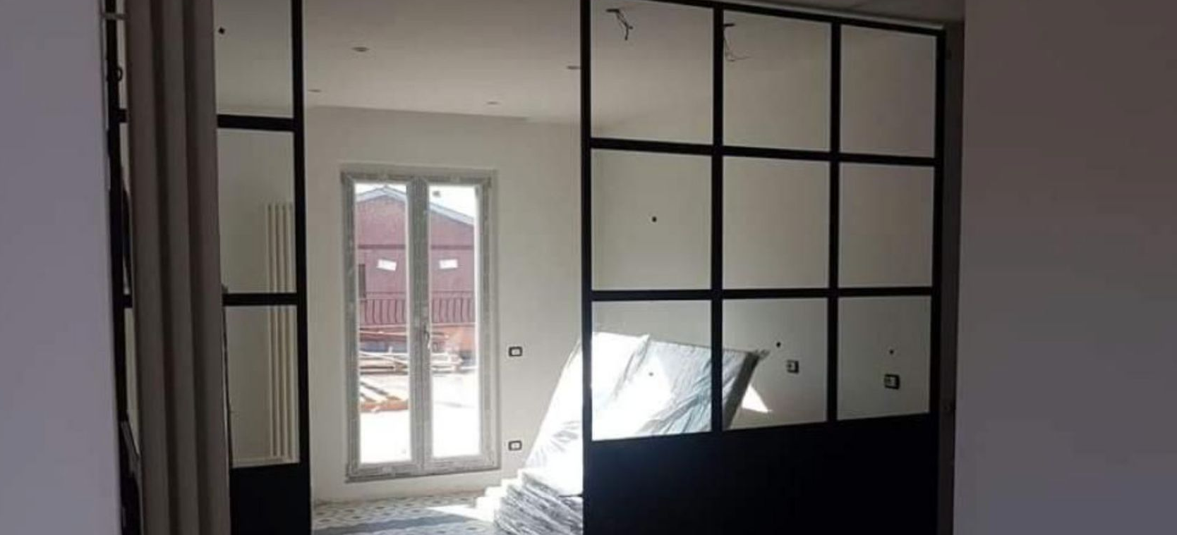 Stanza vuota con un'ampia parete divisoria in vetro con cornice nera e porte finestre che danno su un balcone.