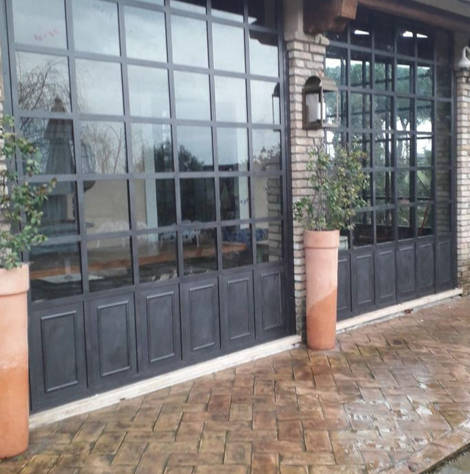 Negozio con vetrina, finestre e porte con telaio nero, muro in mattoni e marciapiede in mattoni bagnati sotto un ingresso coperto.