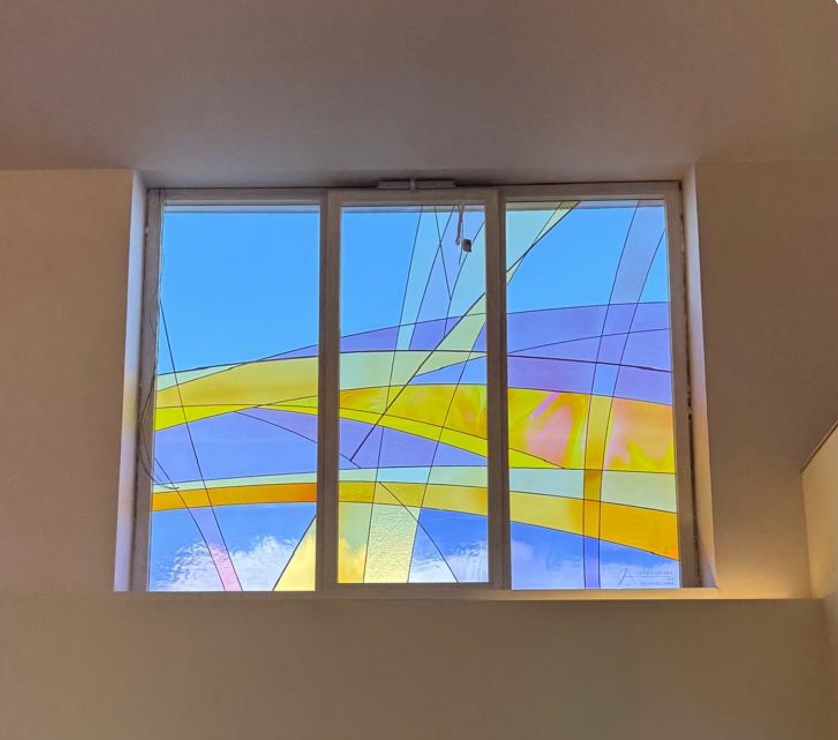 Vetrata astratta e colorata con curve blu, gialle e rosa su uno sfondo beige.