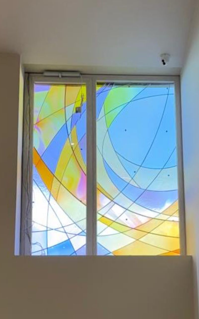 Vetrata astratta e colorata con ampi archi blu, gialli e verdi in una cornice bianca
