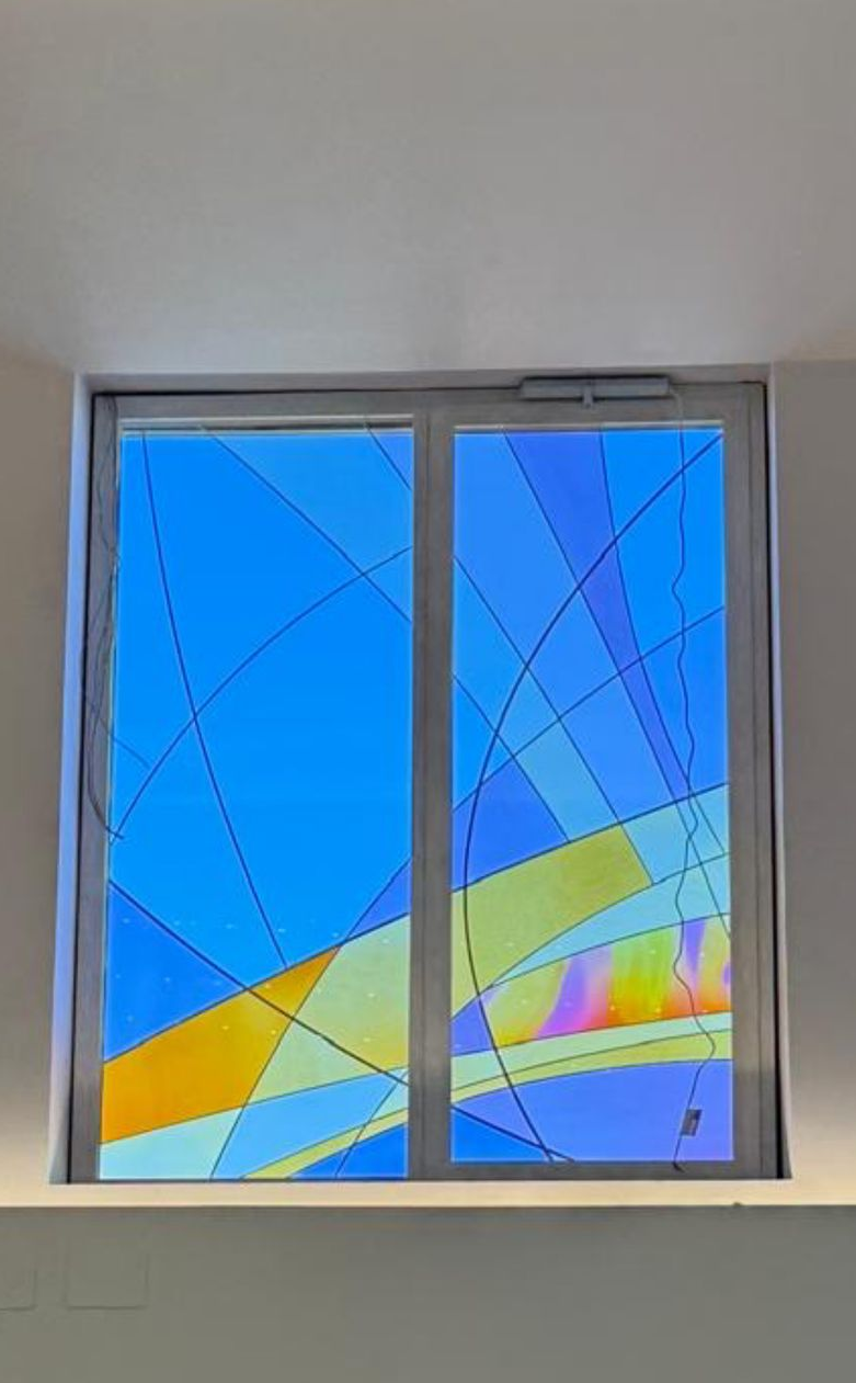 Vetrata astratta con forme geometriche blu, gialle e rosa in una cornice bianca.