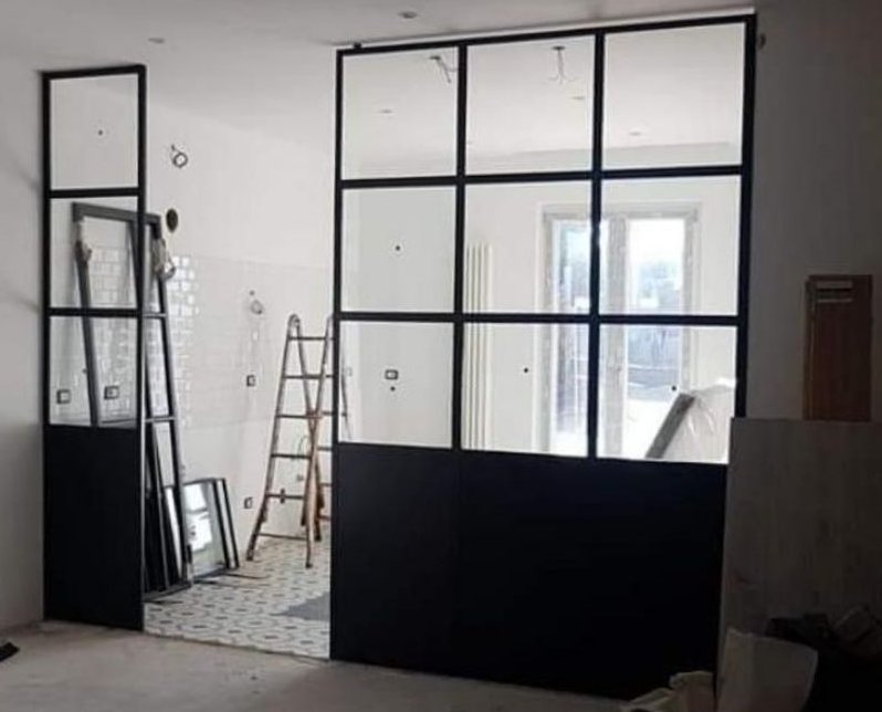 Cantiere di ristrutturazione al chiuso con pareti divisorie in vetro, scala e attrezzi su uno sfondo bianco.