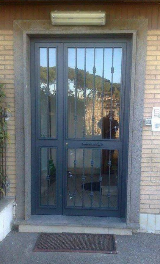 Ingresso di un edificio in mattoni con porta blindata in metallo scuro, pannelli in vetro e applique a parete soprastante.