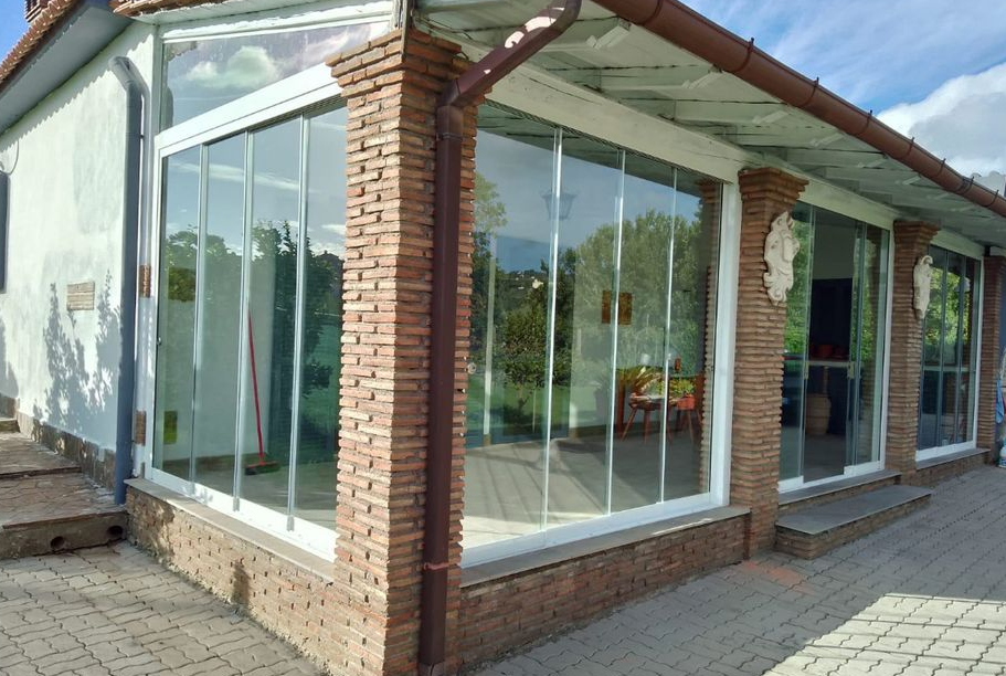 Vetrina angolare con pareti in vetro, colonne in mattoni e porte scorrevoli su un vialetto pavimentato.