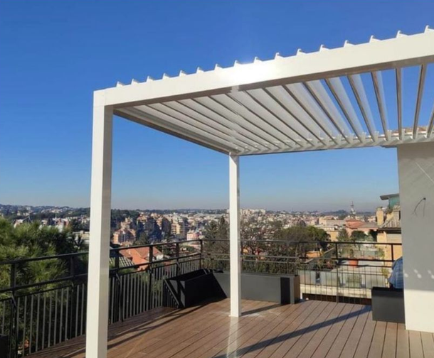 Terrazza sul tetto con pergola bianca, pavimentazione in legno e panorama cittadino sotto un cielo azzurro limpido.