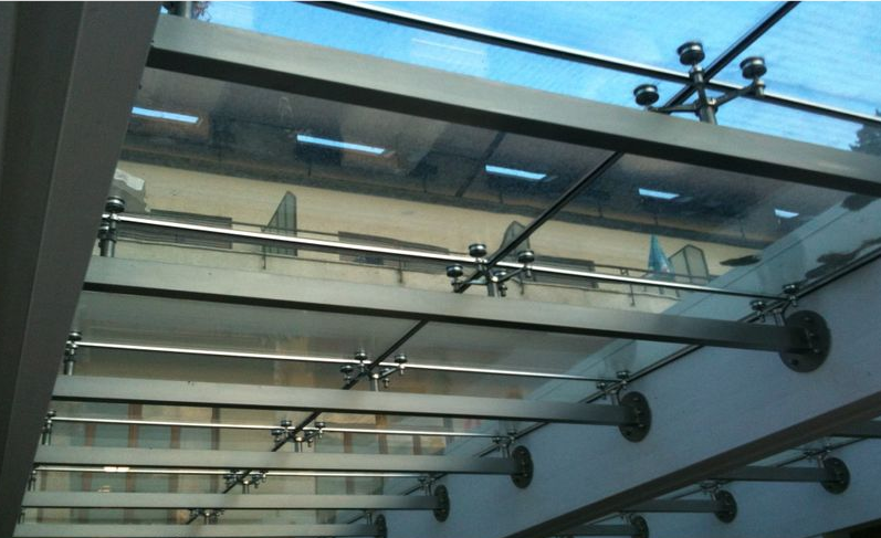 Soffitto dell'atrio in vetro con travi metalliche e diverse lampade a sospensione.