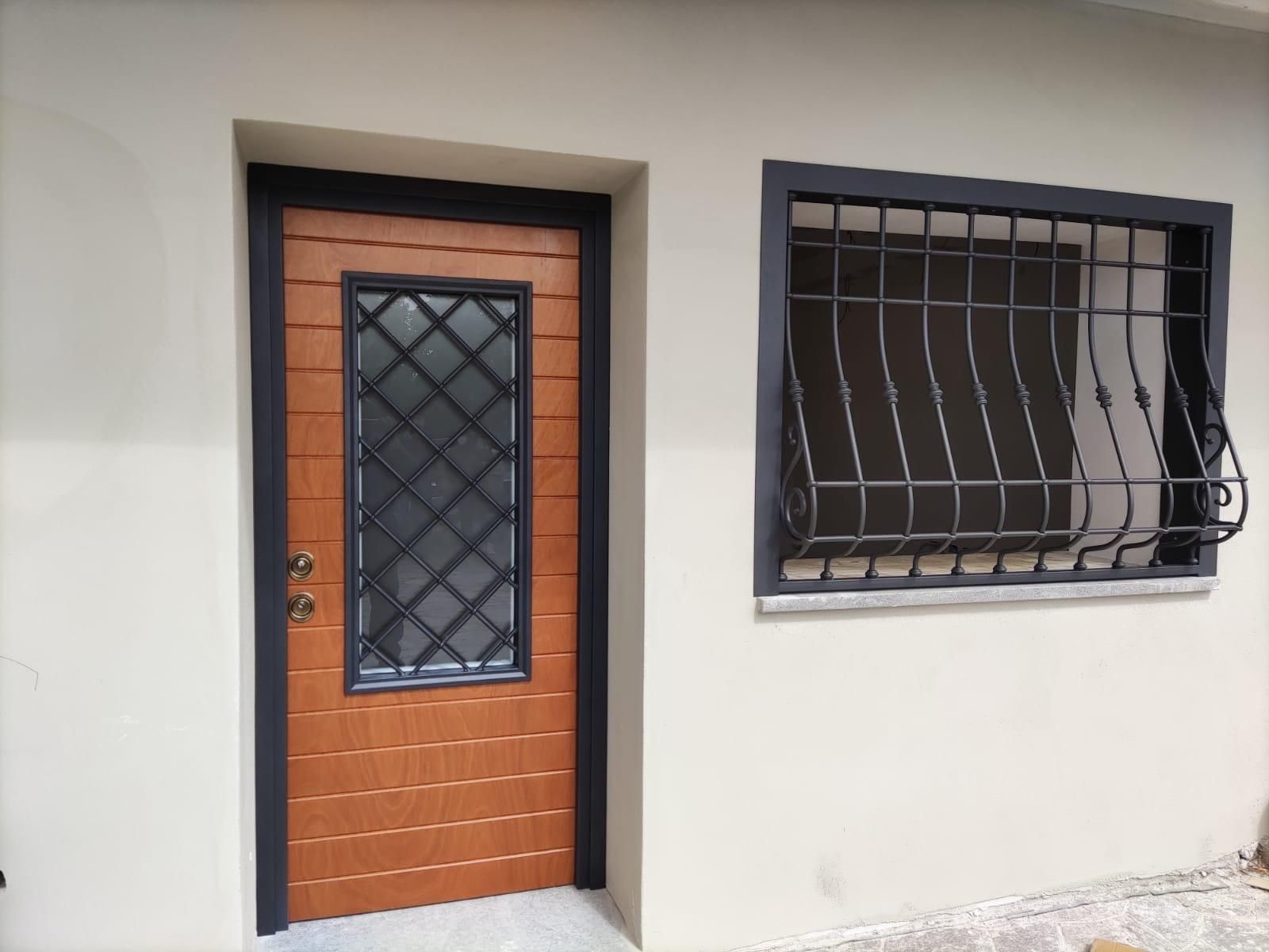Porta d'ingresso con pannello arancione e finestra nera, accanto a una finestra con sbarre su una parete esterna chiara.