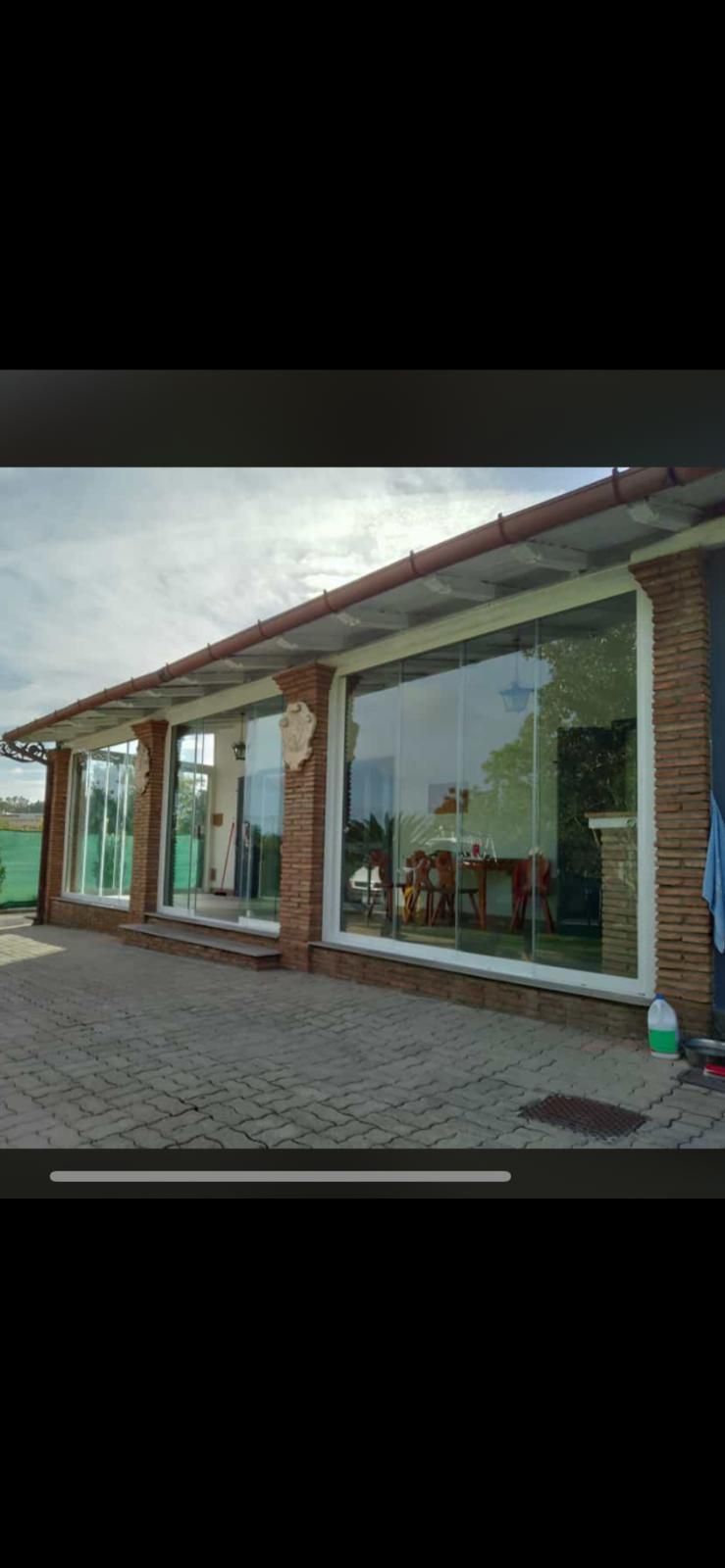 Negozio moderno con facciata in vetro, colonne in mattoni e tetto spiovente, adiacente a un vialetto pavimentato.