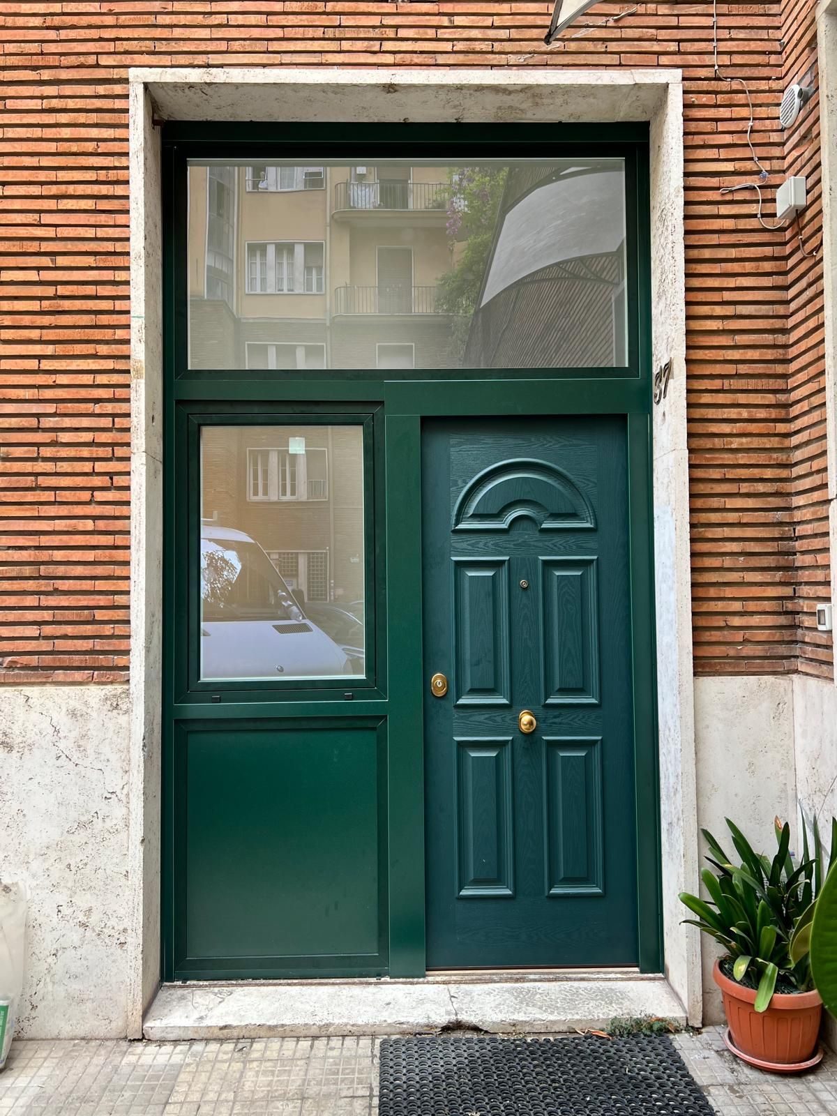 Porta e finestra di colore verde scuro sulla facciata di un edificio in mattoni, con una pianta in vaso accanto.