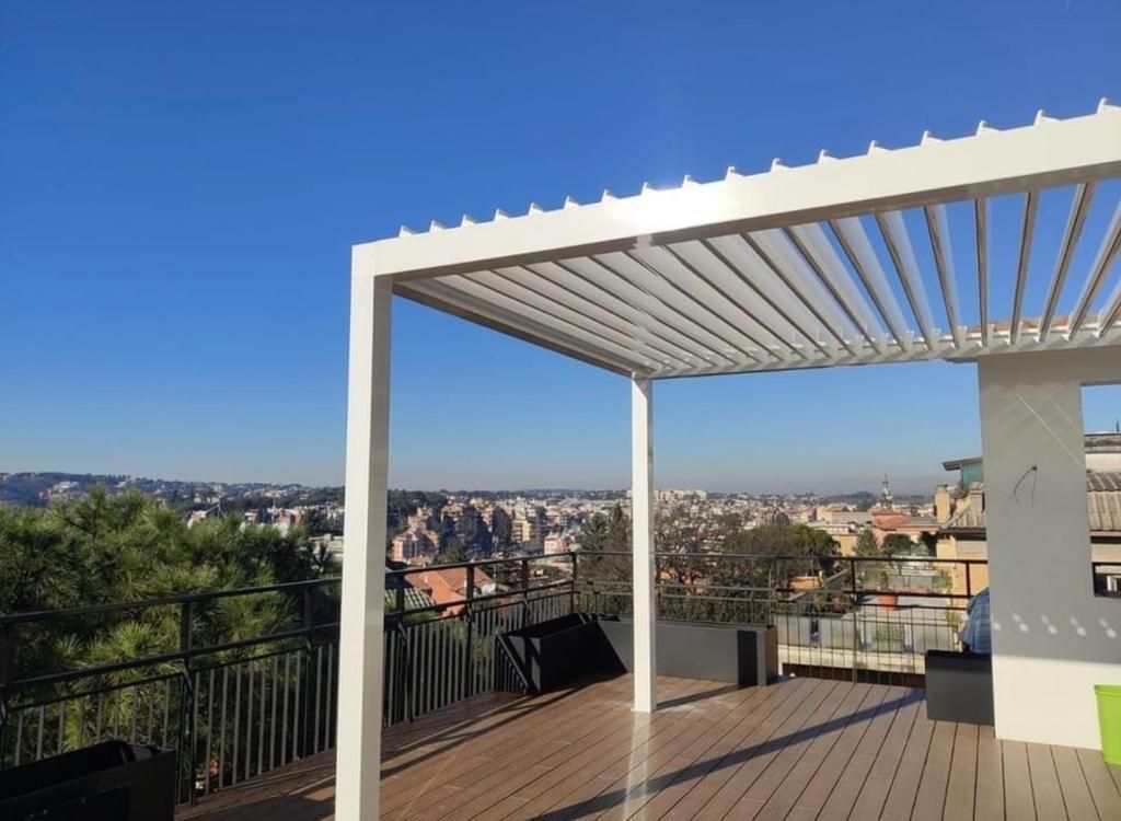 Terrazza sul tetto con pergola bianca che si affaccia sullo skyline della città e sulle colline in lontananza, sotto un cielo azzurro e limpido.