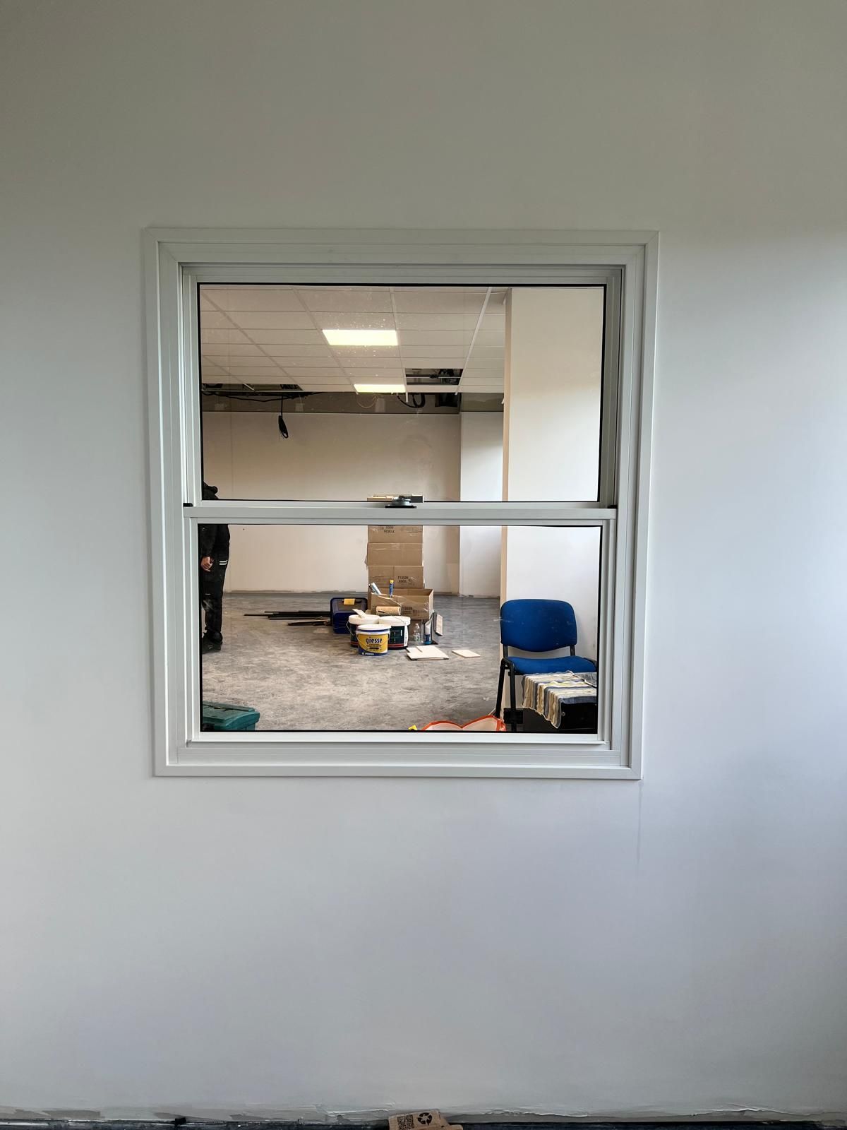Vista dalla finestra su un ufficio con sedie, scatole e lampade a soffitto all'interno di una parete bianca.