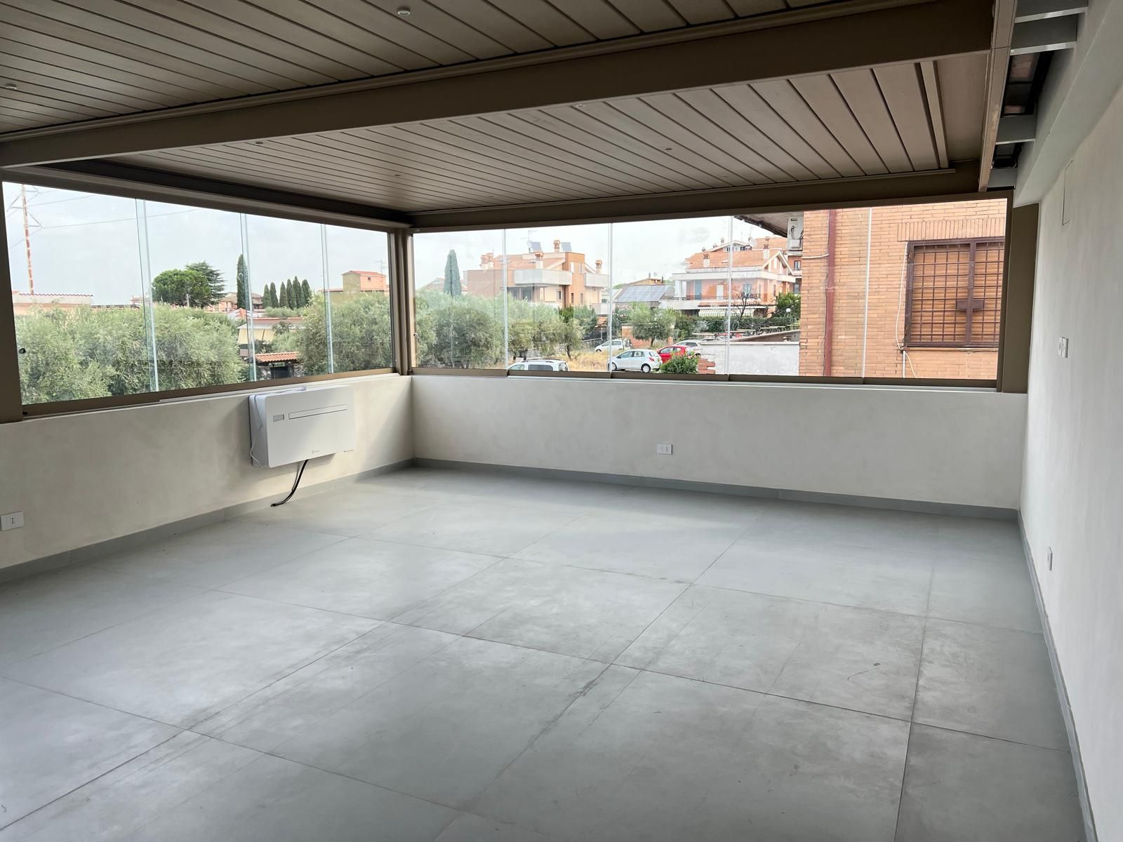 Patio coperto e vuoto con pavimento grigio, pareti bianche e vista aperta sulle case vicine.