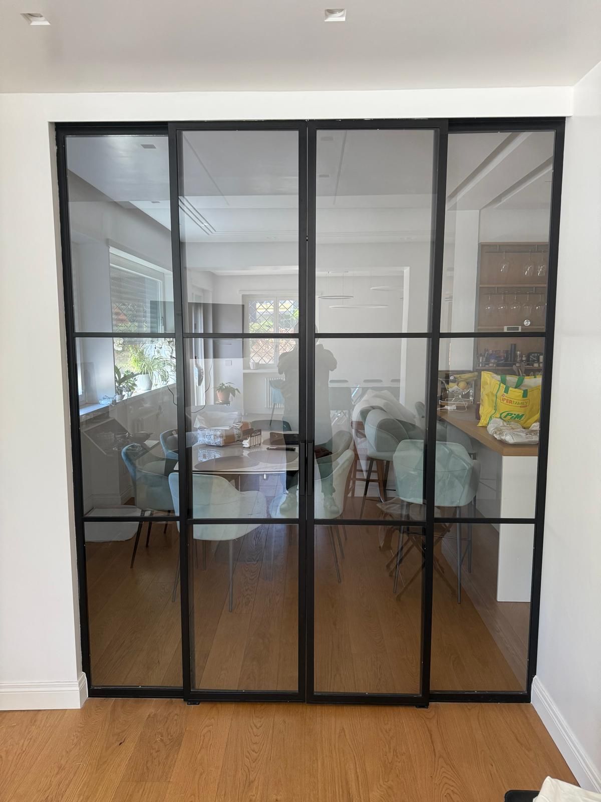 Porte a vetri con cornice nera che si affacciano su una luminosa sala riunioni con tavolo e sedie.