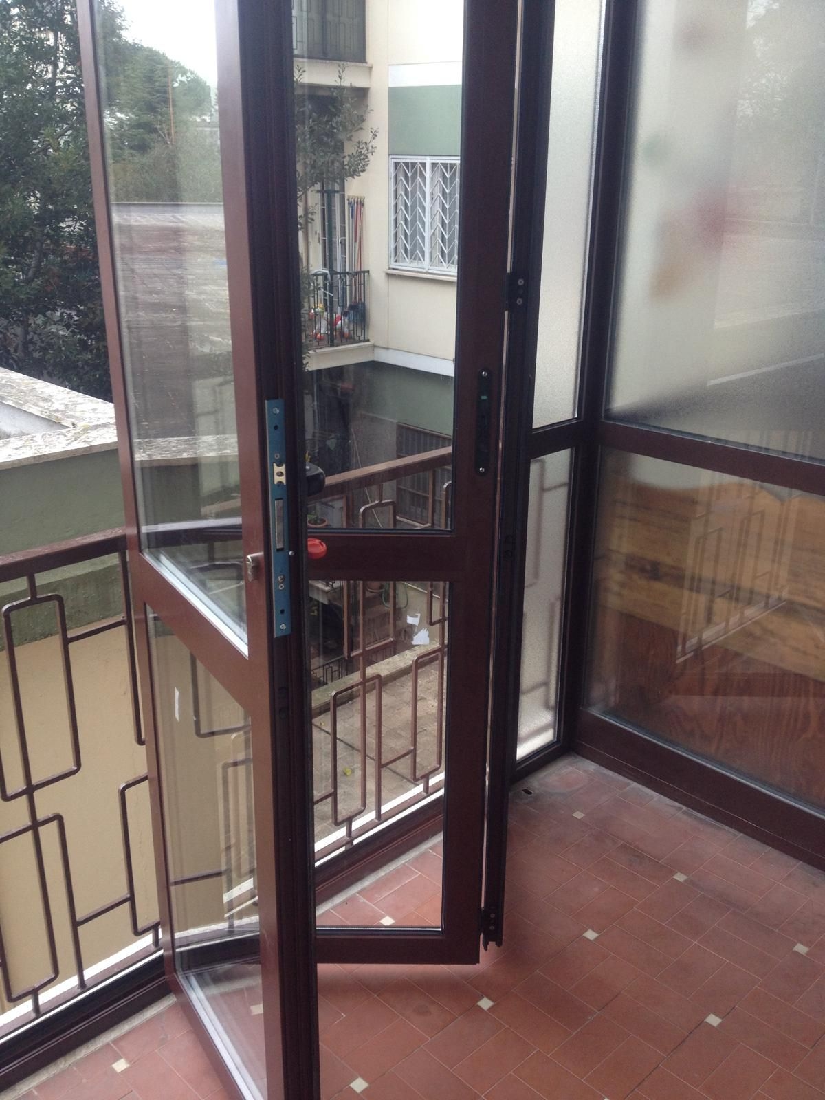Porta finestra apribile con ringhiera in metallo che si affaccia sugli edifici circostanti e su un cortile interno.