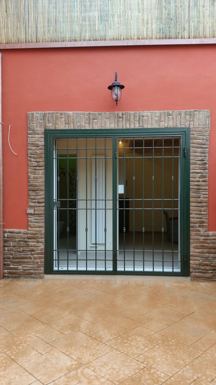 Ingresso principale con cancello di sicurezza in metallo, finiture in mattoni, muro rosso e patio piastrellato.