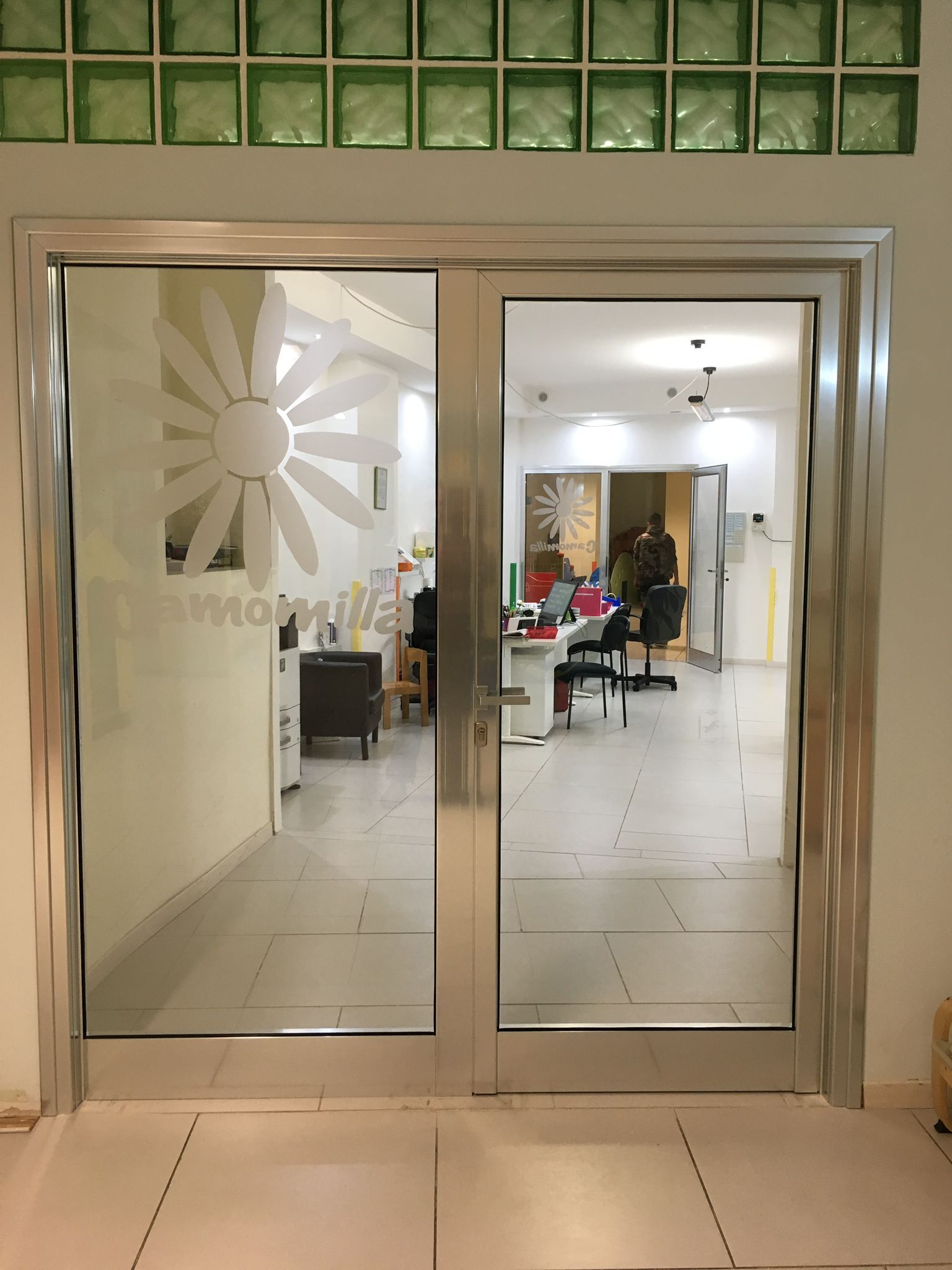 Doppie porte a vetri che conducono a un luminoso salone o ufficio con persone all'interno