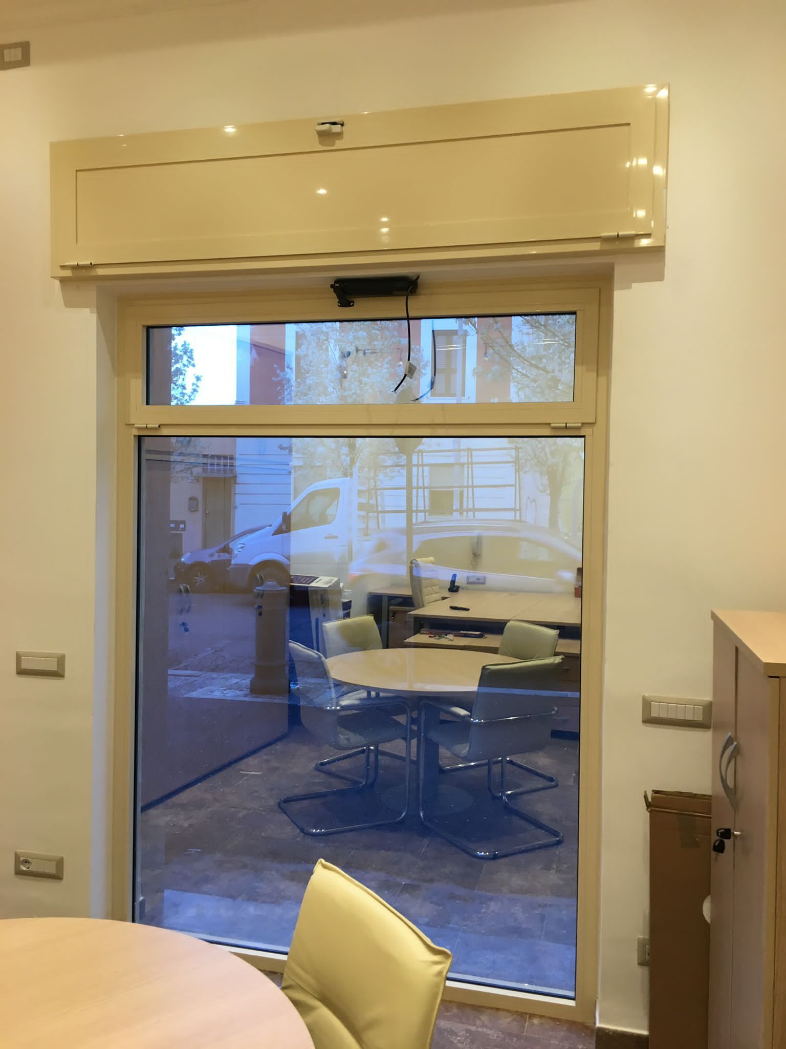 Vista interna attraverso una porta a vetri di una stanza con tavoli, sedie e grandi finestre.