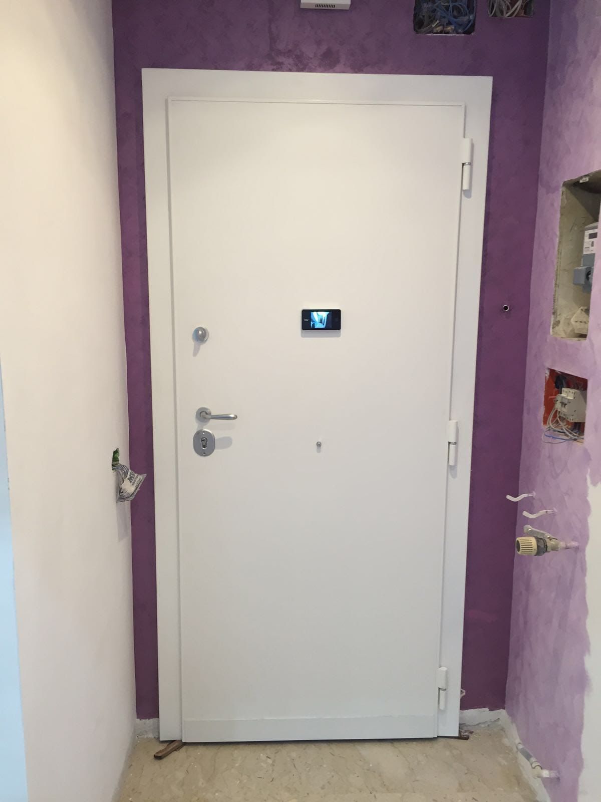 Porta bianca con spioncino e maniglia incastonata in una parete viola del corridoio.