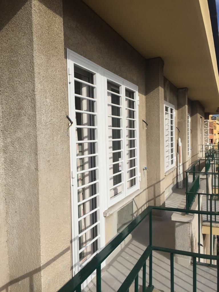 Balcone dell'appartamento con porte finestre bianche, pareti in stucco beige e ringhiere verdi lungo il corridoio.