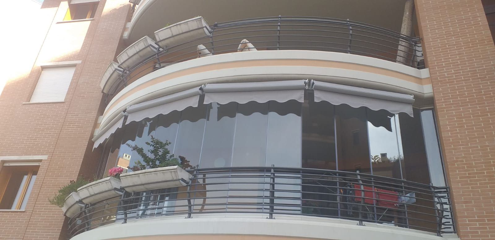 Balcone di un appartamento con tende da sole su un edificio in mattoni, visto dal basso.