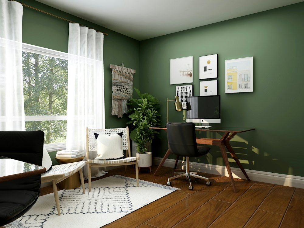 Home office with green walls, a desk, and a chair in soft daylight