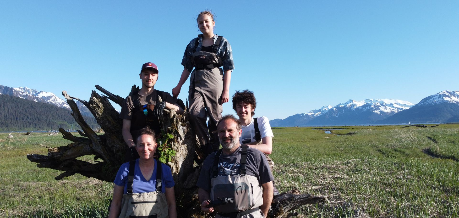 Five people in waders posing in front of mountains.