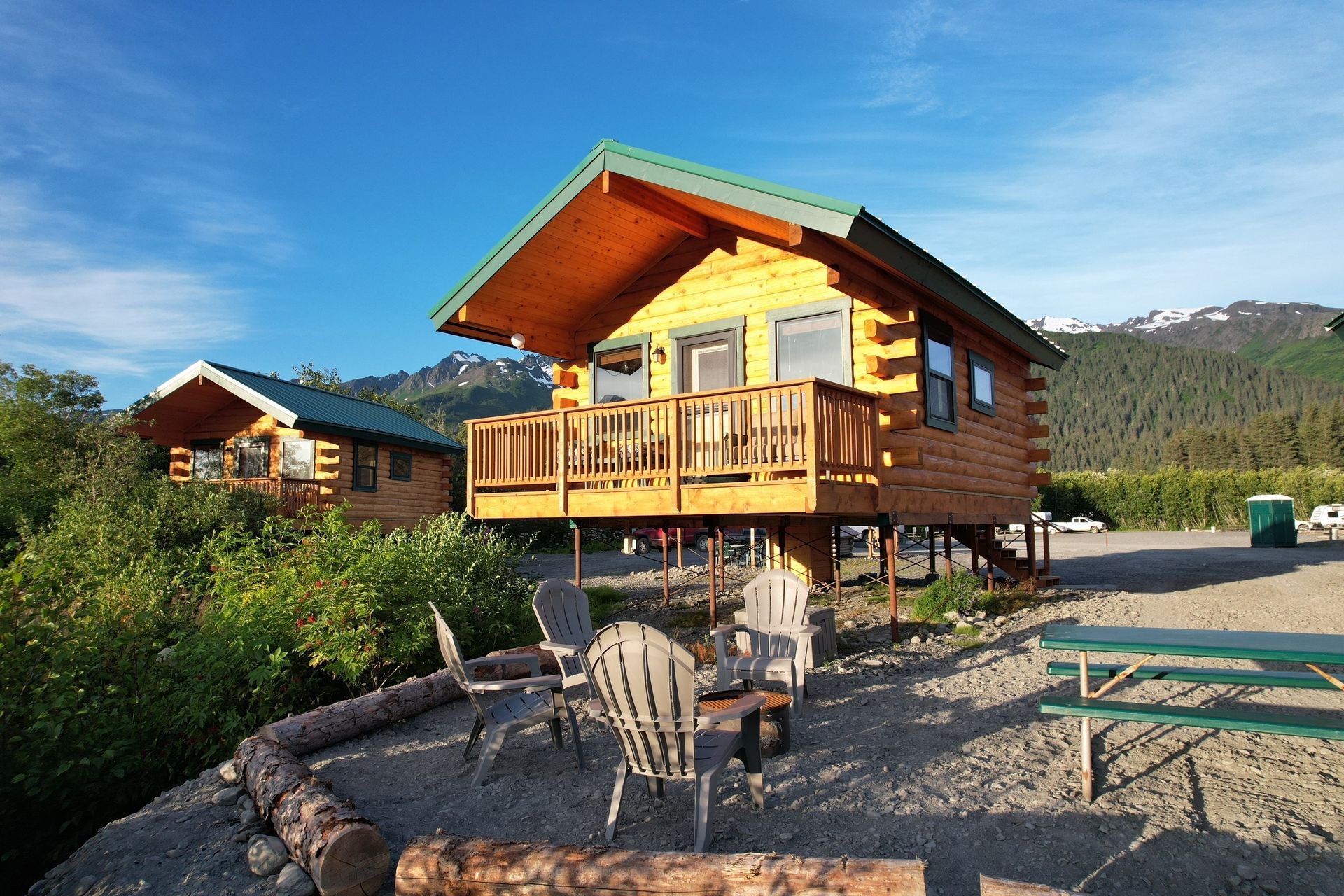 Two wooden cabins with green roofs and balconies on a hillside.